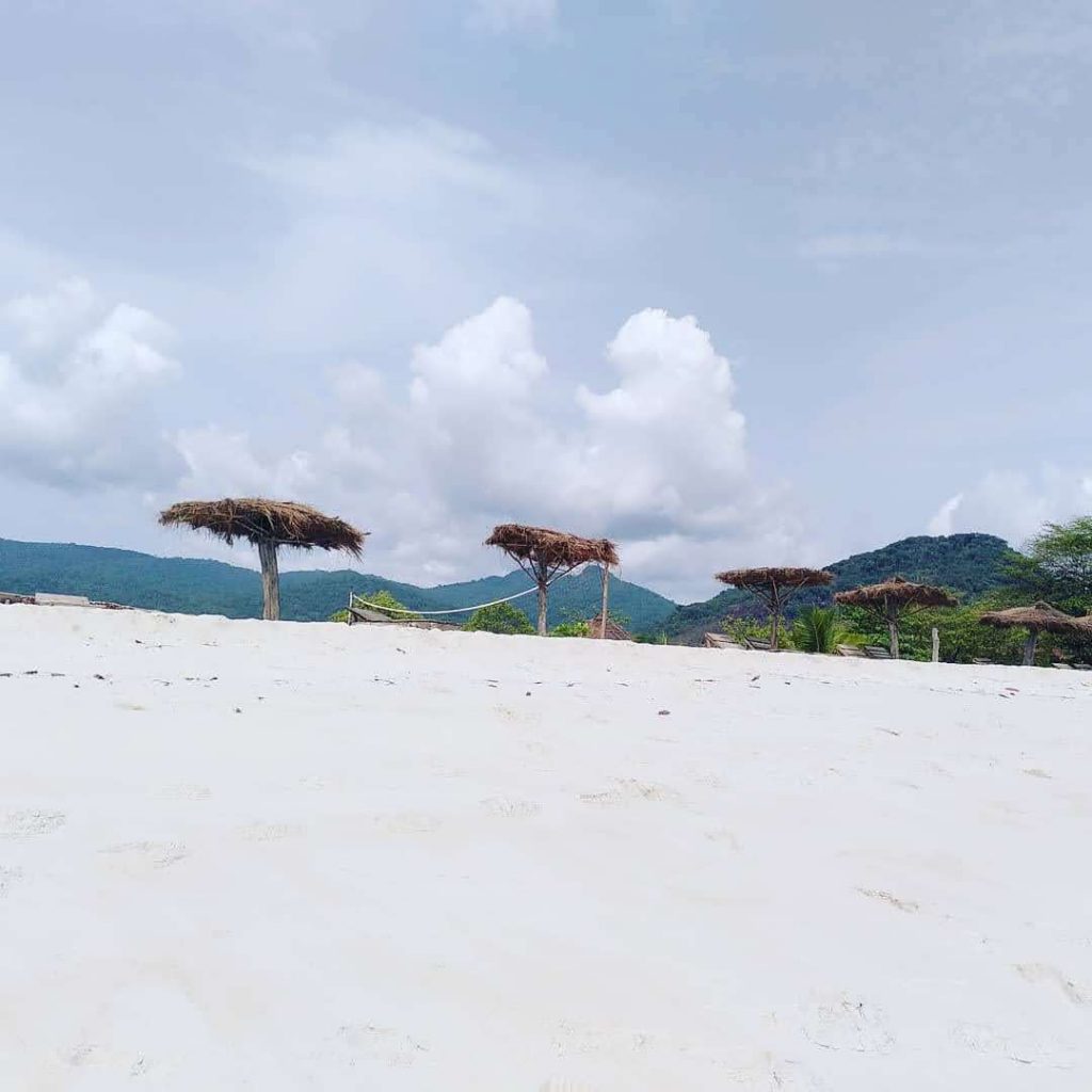 Strand, Strandschirme und grüne Hügel im Hintergrund